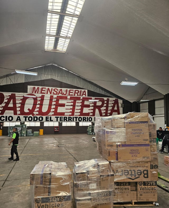 Tarimas envueltas en plástico dentro de un espacio amplio con señalización mural